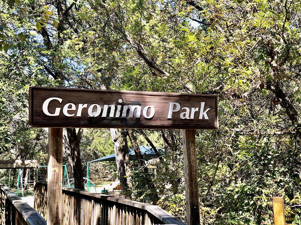 Wooden Geronimo Park entrance sign above the walkway leading into the shaded children’s playground in Apache Shores.