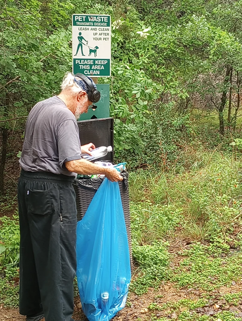 A daily hiker on the Indian Creek Hiking Trail who volunteers to collect trash on his daily walk. Here he is putting trash into a larger trash bag so it can be emptied. Most of the trash is plastic drink bottles.