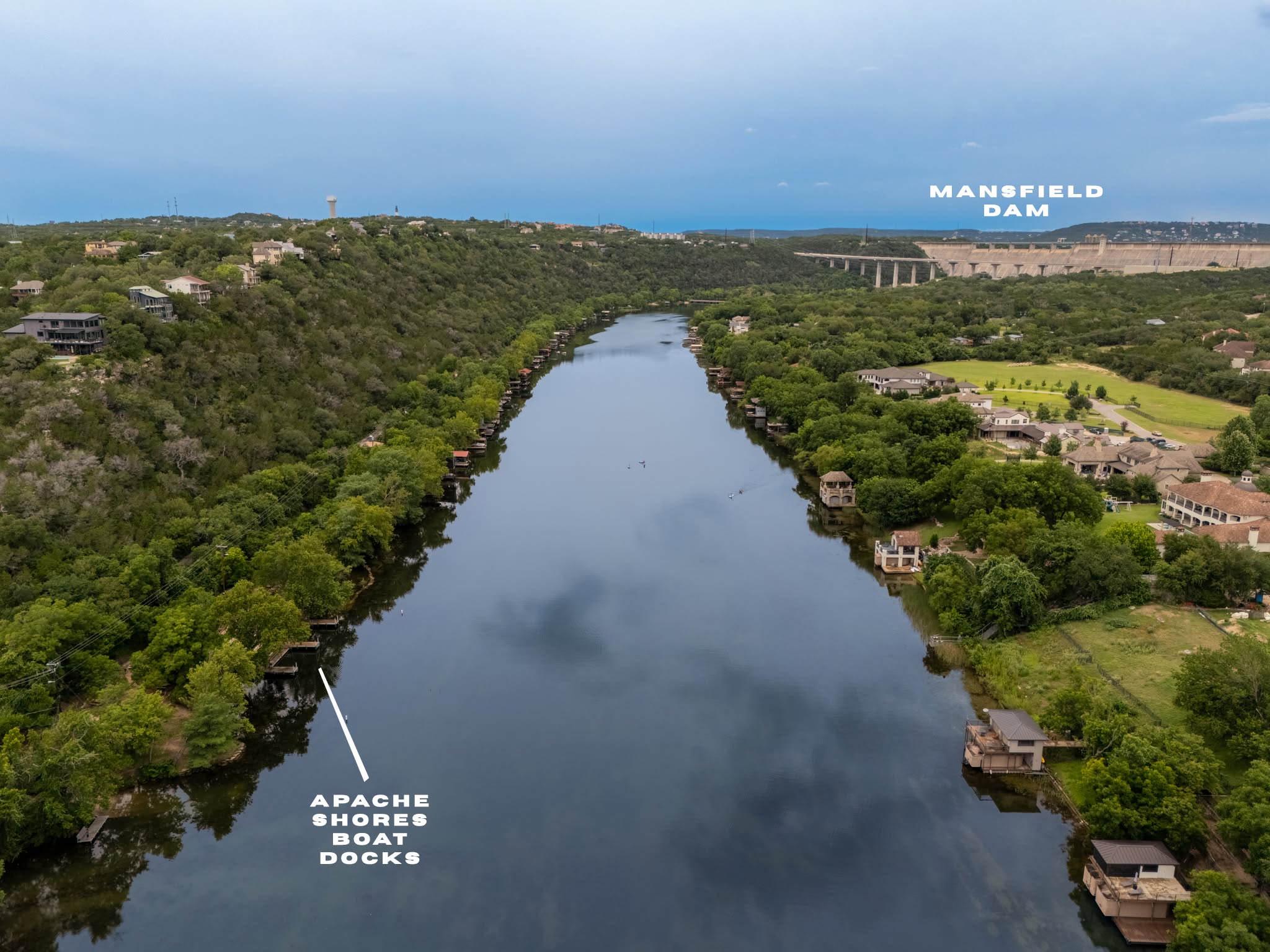 Aerial view of the dock at Lakeside Park extending into Lake Austin, with the tree-lined shoreline and surrounding Hill Country landscape visible from above.