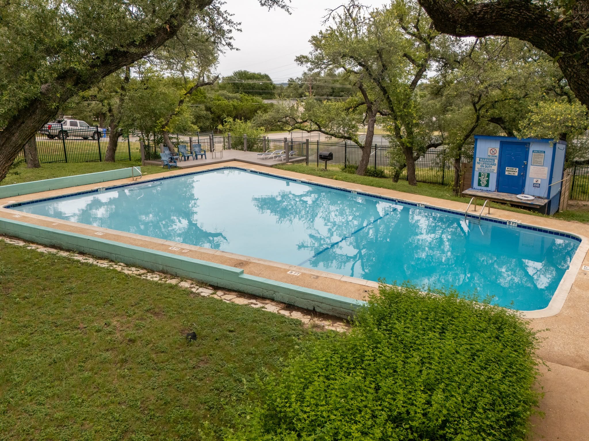 Aerial view of the Apache Shores swimming pool and surrounding pool deck, nestled among mature trees in the wooded neighborhood.